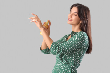 Beautiful young woman applying face foundation on hand on grey background