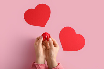Female hands with red fortune cookie and paper hearts on pink background