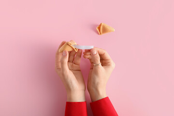 Female hands with broken fortune cookie on pink background