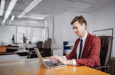 A young businessman in an office setting, using a laptop