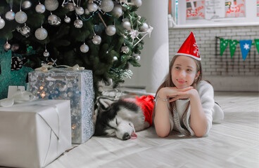 A young girl and her dog are enjoying the holiday gifts by the tree.