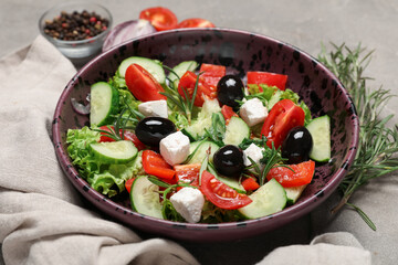 Bowl of tasty Greek salad, rosemary and napkin on grunge table