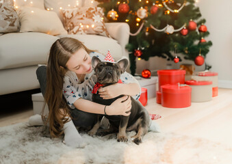 In a joyful and loving moment, a young girl and her dog smile together against a background of Christmas decorations.