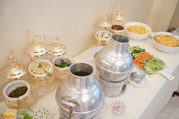 A beautifully arranged traditional Saudi Arabian buffet featuring classic Middle Eastern dishes, fresh vegetables, and traditional soup served in metal jugs. The golden serving bowls add an elegant to