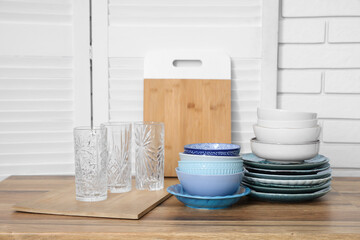Glasses, stacks of plates and bowls on table near white brick wall in kitchen