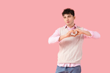 Handsome young man making heart gesture and blowing kiss on pink background