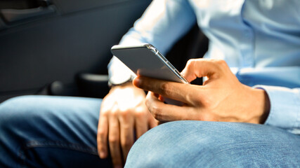 Unrecognizable man in formal outfit using cellphone while going to office by taxi or corporate car, checking emails or chatting with assistant, closeup shot, panorama with copy space