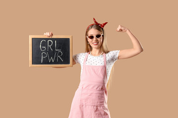 Young pin-up woman holding chalkboard with text GRL PWR and showing muscles on beige background....