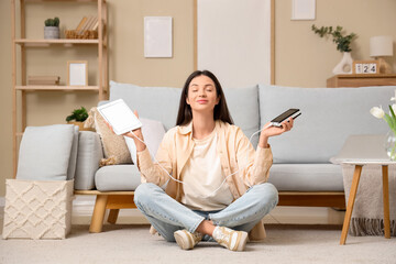Beautiful young woman with modern power bank and tablet computer meditating at home