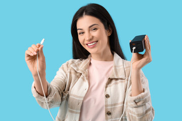 Beautiful young woman with modern power bank on blue background