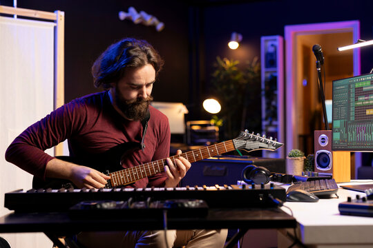 Talented musician playing acoustic guitar while he records tunes on daw software for mixing and mastering session, home studio gear. Skilled artist recording his musical instrument tracks.