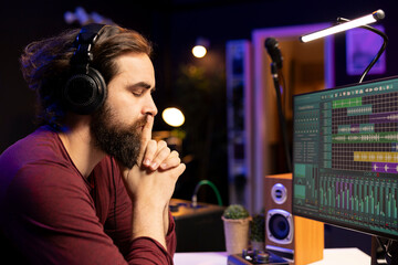 Music producer listening carefully his audio recording after editing and adjusting volume levels in...