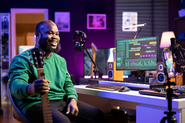 Obraz premium Musical composer hosting online guitar lessons with tutorial video on smartphone, recording himself playing acoustic instrument. Young artist teaching people how to play accords on strings, vlog.