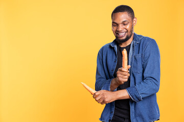 African american funny person fooling around with bio carrots, pretending to play drums instrument in studio. Young silly guy advertising healthy eating and zero waste concept.