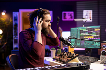 Skilled confident musician editing tunes with daw software on microphone to create tracks with...