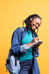 Happy professional brainstorming ideas, writing on document using pen. Upbeat african american photographer using clipboard to complete shoot list for upcoming photography work, studio background