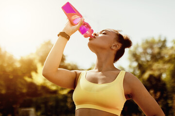 Dehydration After Workout. Sporty African American female wearing yellow top drinking mineral water...