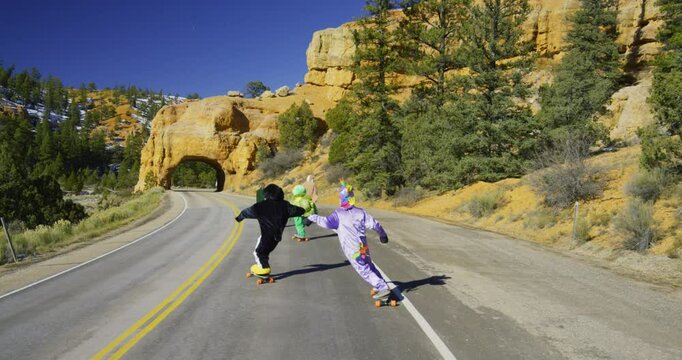 Slow motion following shot of people in costumes riding longboards toward red, stone arch