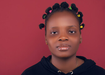 Portrait of a young woman with colorful Bantu knots, wearing a black hoodie, gazing calmly at the...