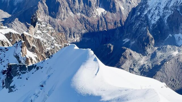 Paragliders with backpacks descend the steep snowy slopes of Aiguille du Midi, Chamonix, preparing for a parachute jump between the majestic peaks of the French Alps, with amazing view of Mont Blanc