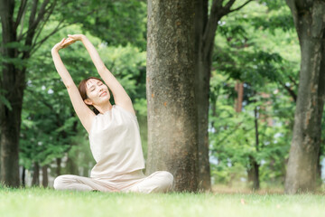 森・公園でパークヨガ・ヨガ・ピラティス・ストレッチをする若いアジア人女性
