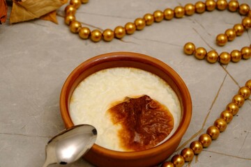 The flavor of Turkish cuisine is baked rice pudding in a casserole. Metal spoon next to it. Decorative presentation with gold beads and dried rose. Homemade rice pudding. Ramadan table.
