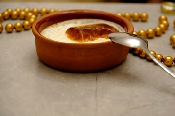 The flavor of Turkish cuisine is baked rice pudding in a casserole. Metal spoon next to it. Decorative presentation with gold beads and dried rose. Homemade rice pudding. Ramadan table.
