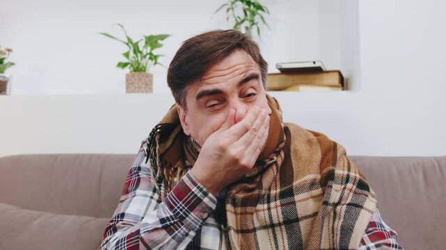 An elderly man, wrapped in a cozy blanket sneezing, coughing and fighting off a cold in a bright living room filled with plants and cozy decor.