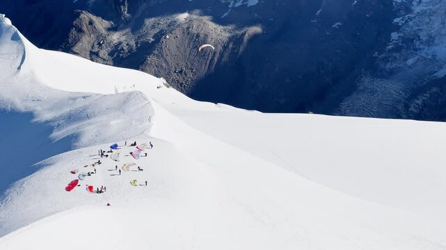 Paragliders with backpacks descend the steep snowy slopes of Aiguille du Midi, Chamonix, preparing for a parachute jump between the majestic peaks of the French Alps, with amazing view of Mont Blanc