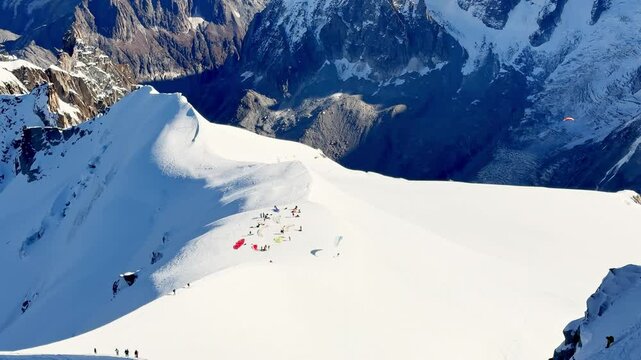 Paragliders with backpacks descend the steep snowy slopes of Aiguille du Midi, Chamonix, preparing for a parachute jump between the majestic peaks of the French Alps, with amazing view of Mont Blanc