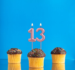 Birthday candle with the number 13 - Three cupcakes on a blue background.