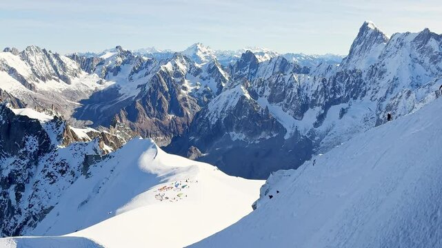 Paragliders with backpacks descend the steep snowy slopes of Aiguille du Midi, Chamonix, preparing for a parachute jump between the majestic peaks of the French Alps, with aamazing view of Mont Blanc