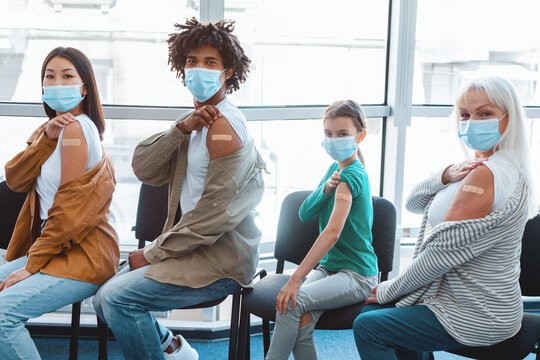 Vaccinated multiethnic people in face masks showing shoulders with adhesive bandage after getting covid vaccine, sitting in line at clinic. Group of men and women with band-aids received injection
