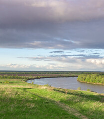 River runs through a grassy field with a cloudy sky in the background