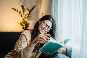 Young caucasian woman reading book or learning by the window	