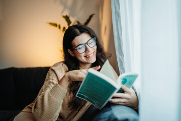 Young caucasian woman reading book or learning by the window 