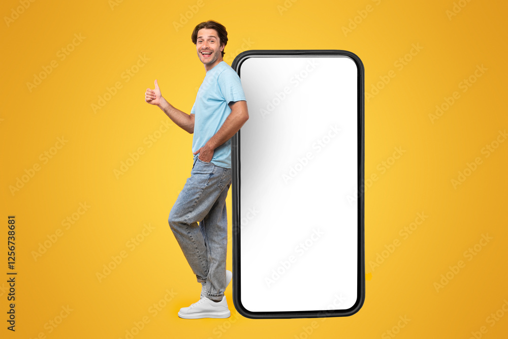 Poster excited man leaning on big smartphone with blank white screen and gesturing thumb up sign, cheerful 