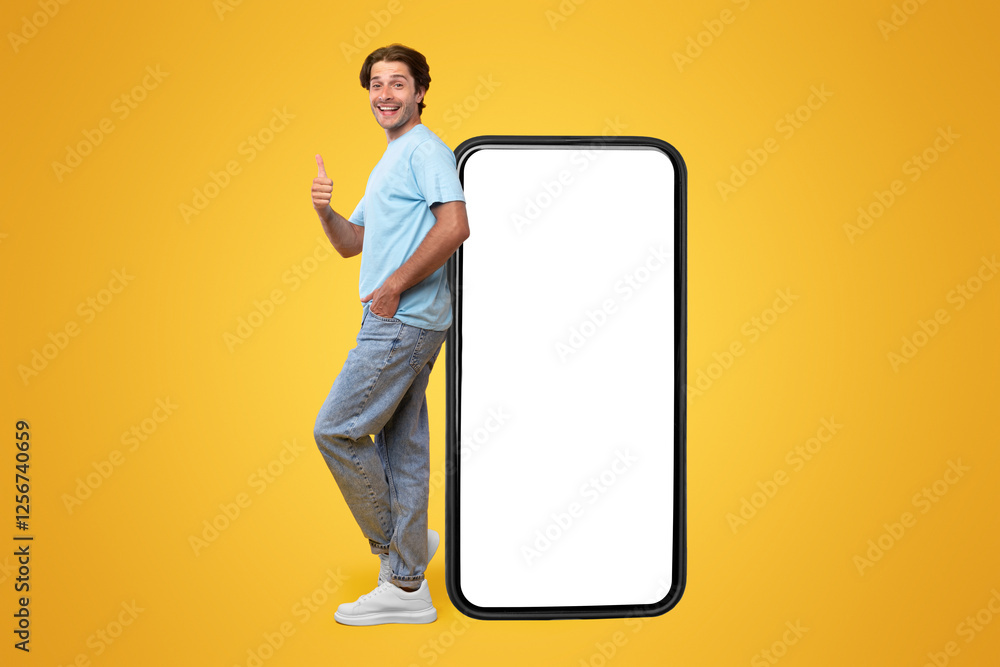 Poster cheerful young man standing leaning on big huge new cell phone with white empty screen and showing t