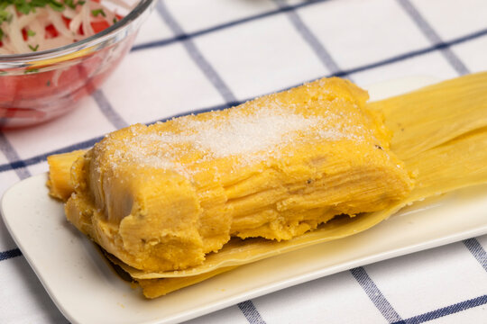 detalle de humitas en hojas con azucar, plato t&iacute;pico Chileno en Verano, junto a ensalada de tomate con cebolla