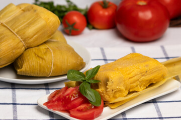Humitas en hojas, plato típico Chileno en Verano, junto a ensalada de tomate, al fondo tomates...