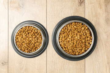 Dry pet food in feeding bowls on wooden floor, top view