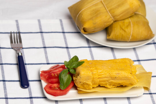 Humitas en hojas, plato t&iacute;pico Chileno en Verano, junto a ensalada de tomate y al fondo 2 humitas sin abrir