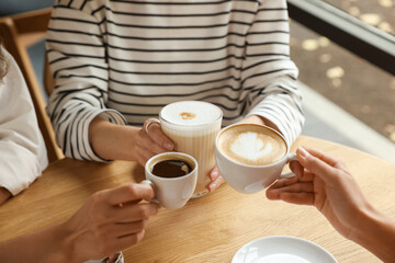 Women with cups of delicious coffee drinks at wooden table in cafe, closeup