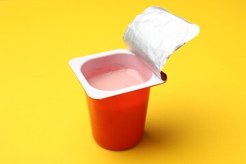 Delicious yogurt in plastic cup on yellow background, closeup