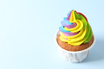 Tasty cupcake with colorful cream on light blue background, closeup. Space for text