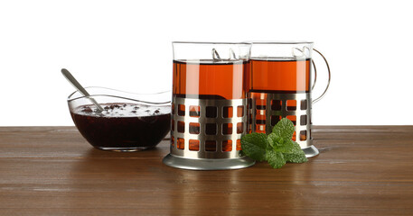 Glasses of aromatic tea in holders, mint and jam on wooden table against white
