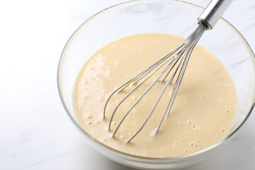 Whisk and bowl of dough on white marble table, closeup. Space for text