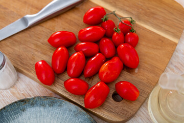 Closeup of fresh ripe red plum-shaped cherry tomatoes prepared for cooking on wooden table with knife and seasonings. Vegetarian food concept..