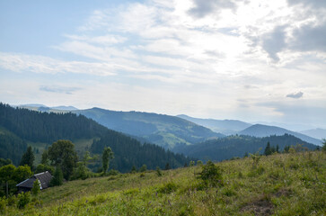 Tranquil mountain scene with rolling hills, verdant trees, and charming rustic house under overcast...