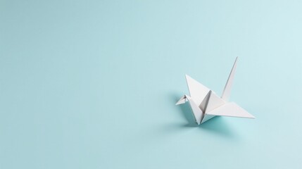Naklejka premium A solitary white origami crane rests on a pale blue background, symbolizing hope, peace, and delicate artistry.